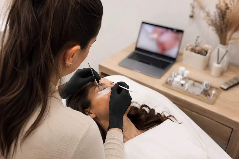 Profissional aplicando lash lifting enquanto assiste ao video da tecnica